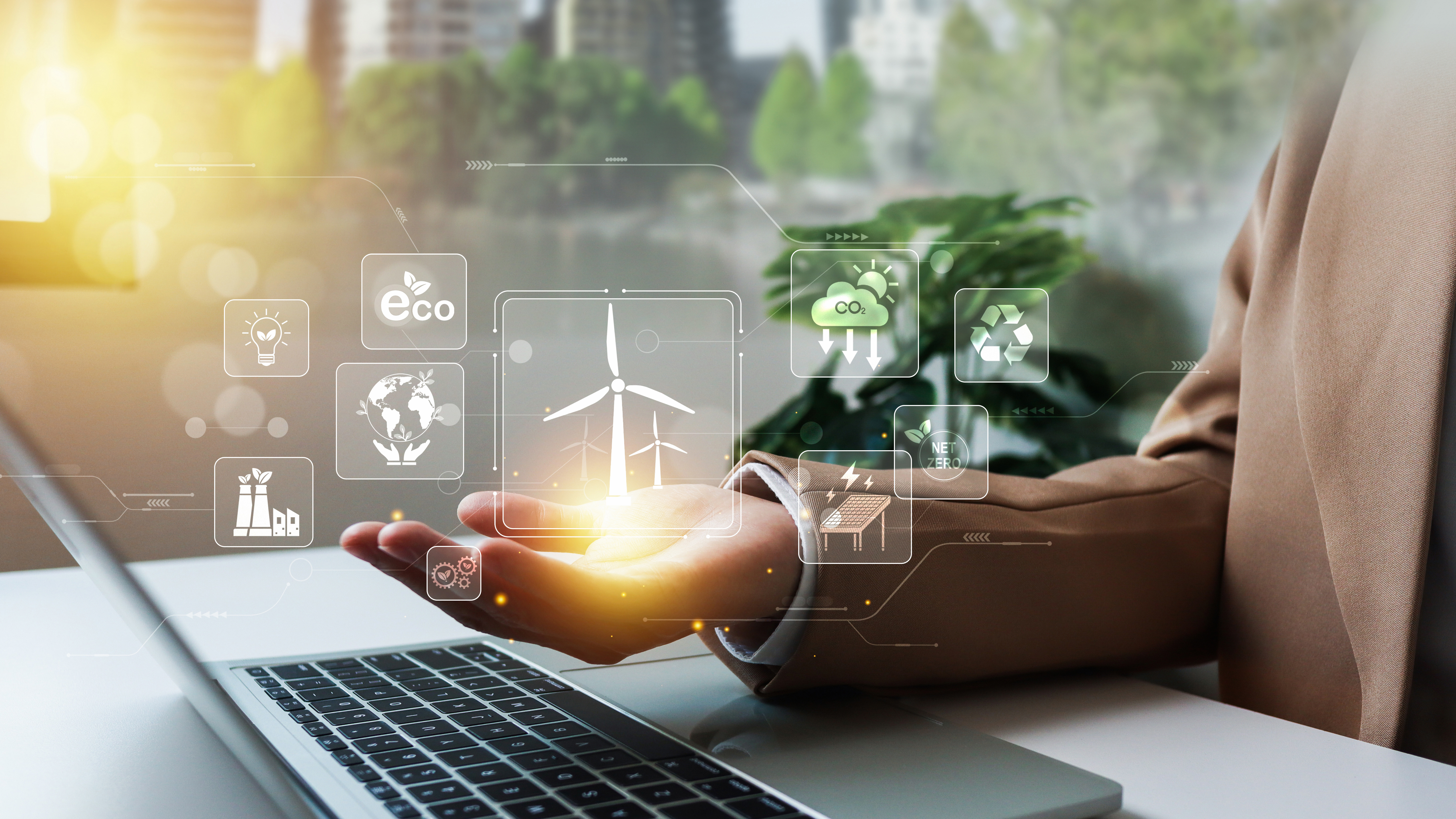 Hand cupped over laptop with digital sustainability images