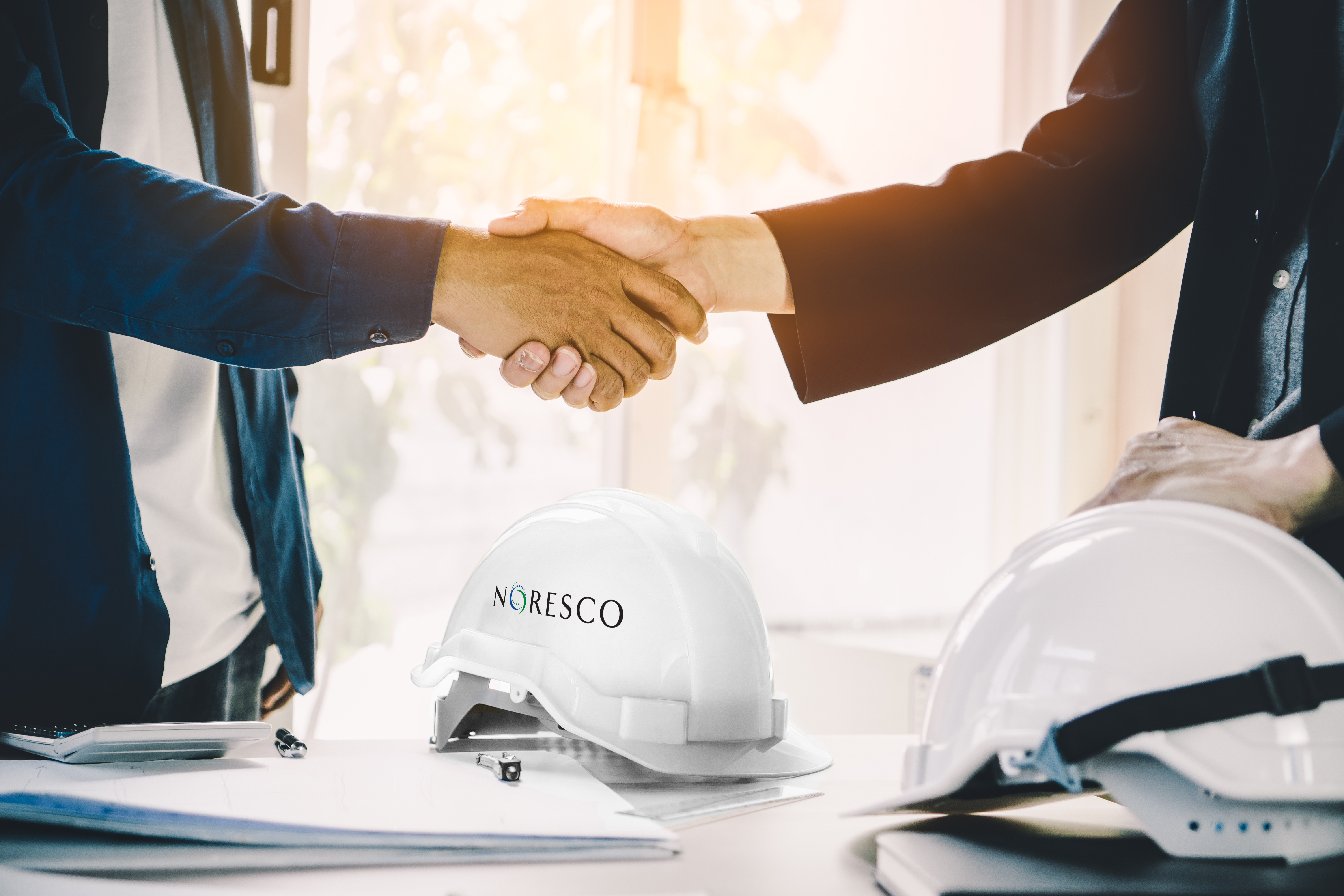 Employees shaking hands over NORESCO hard hat