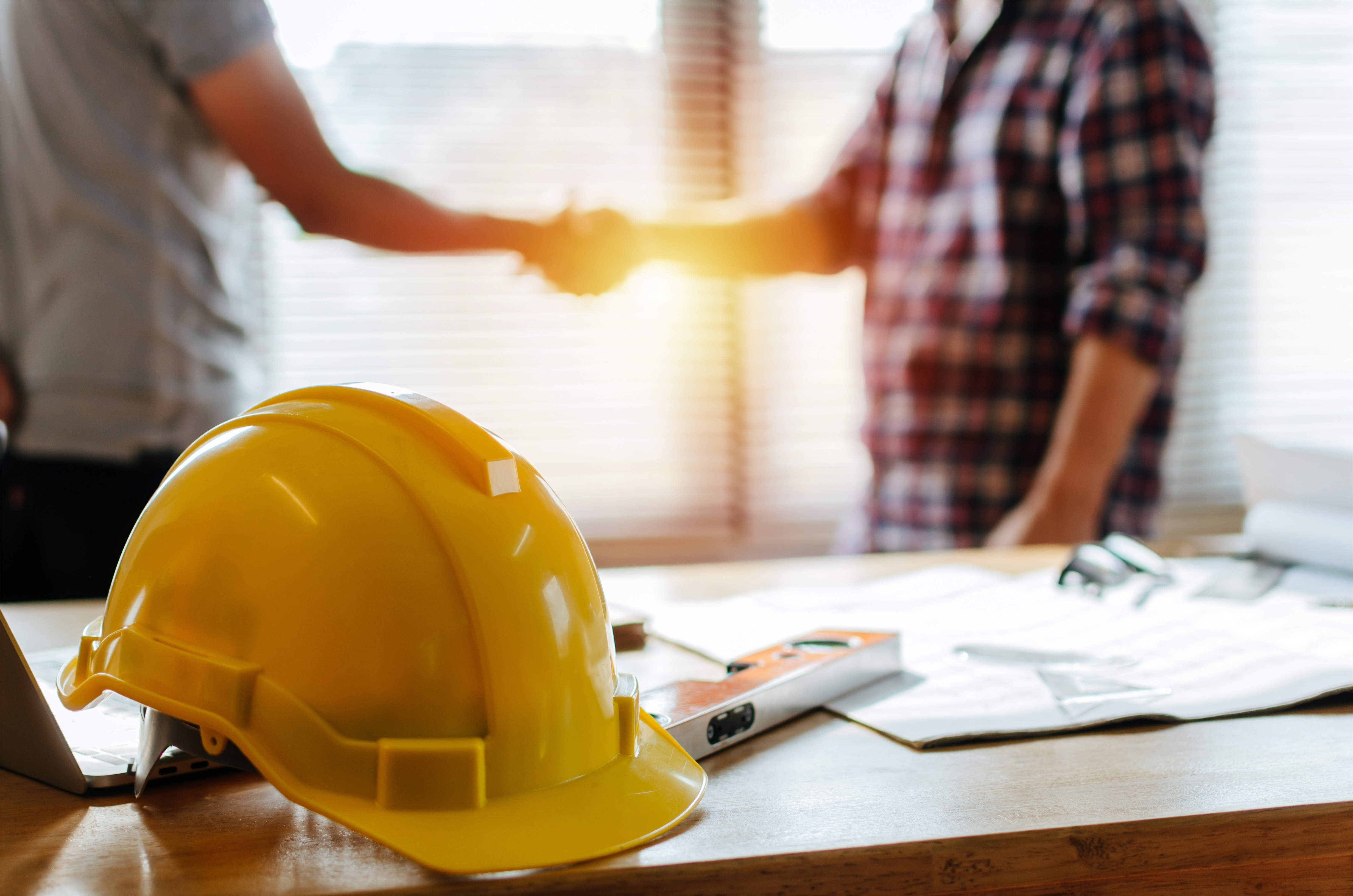 Energineers and construction workers shaking hands behind yellow hard hat